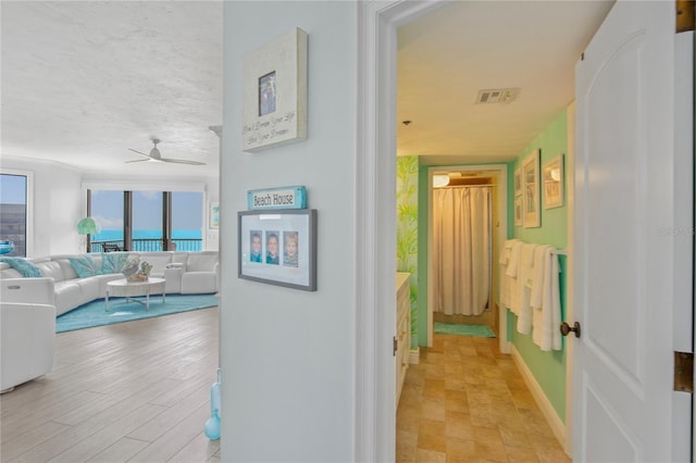 corridor featuring a textured ceiling, visible vents, and baseboards