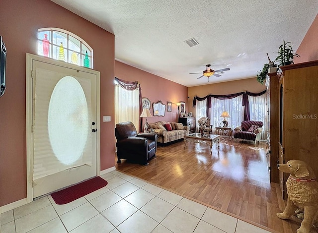 foyer featuring light tile patterned floors, visible vents, a textured ceiling, and a ceiling fan