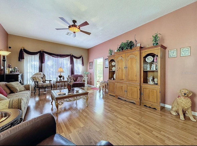 living room featuring visible vents, light wood-style flooring, a ceiling fan, a textured ceiling, and baseboards