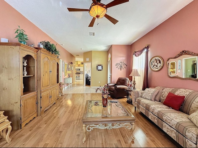 living area featuring ceiling fan, visible vents, light wood finished floors, and a textured ceiling