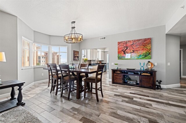 dining area featuring baseboards, visible vents, wood finished floors, a textured ceiling, and a notable chandelier