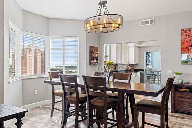 dining area with baseboards, light wood-style floors, visible vents, and an inviting chandelier