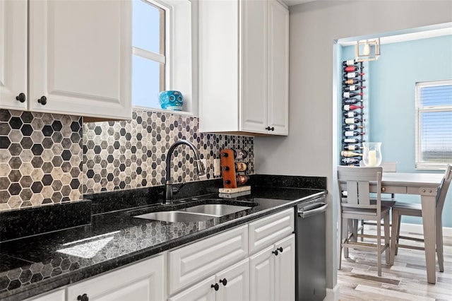 kitchen with decorative backsplash, dark stone counters, light wood-type flooring, white cabinetry, and a sink