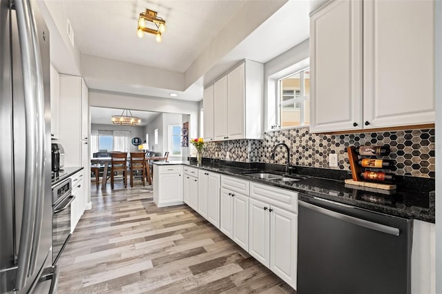 kitchen with light wood finished floors, decorative backsplash, stainless steel appliances, white cabinetry, and a sink