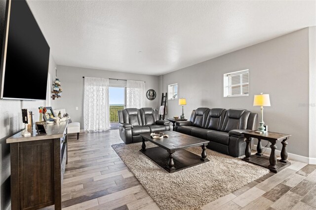 living area featuring a textured ceiling, light wood-style flooring, and baseboards