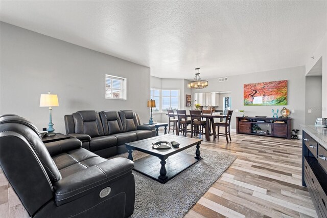 living room featuring a chandelier, light wood-type flooring, visible vents, and a textured ceiling