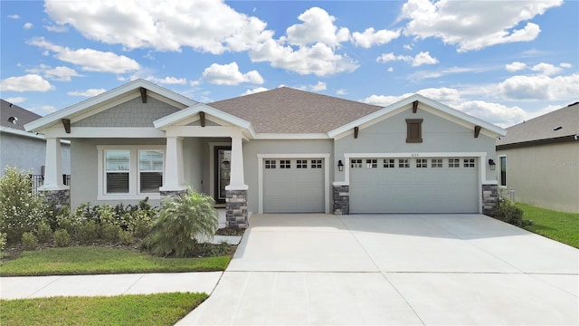 craftsman inspired home with a garage, driveway, stone siding, roof with shingles, and stucco siding