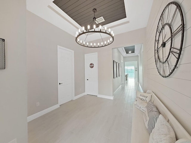 corridor with visible vents, baseboards, light wood-style flooring, a tray ceiling, and a notable chandelier