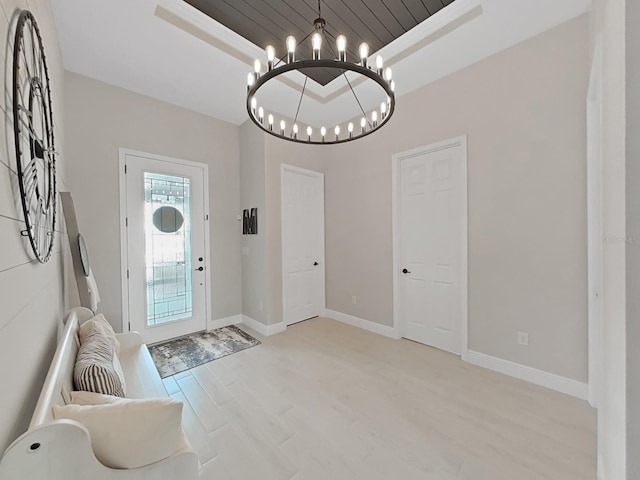 entrance foyer with baseboards, light wood-type flooring, a raised ceiling, and an inviting chandelier