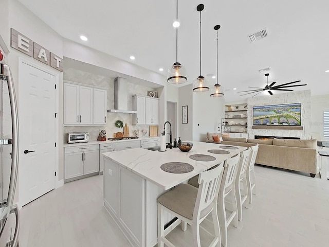 kitchen with visible vents, white cabinetry, wall chimney range hood, and light stone countertops