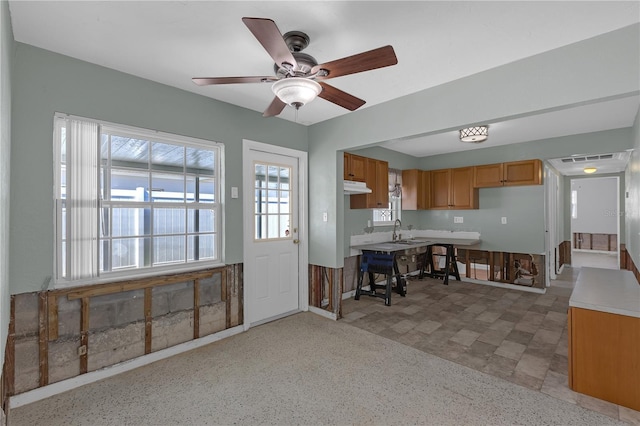 kitchen featuring ceiling fan, under cabinet range hood, a sink, light countertops, and brown cabinetry