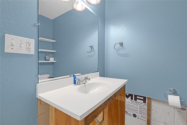 half bath with toilet, a textured wall, and vanity