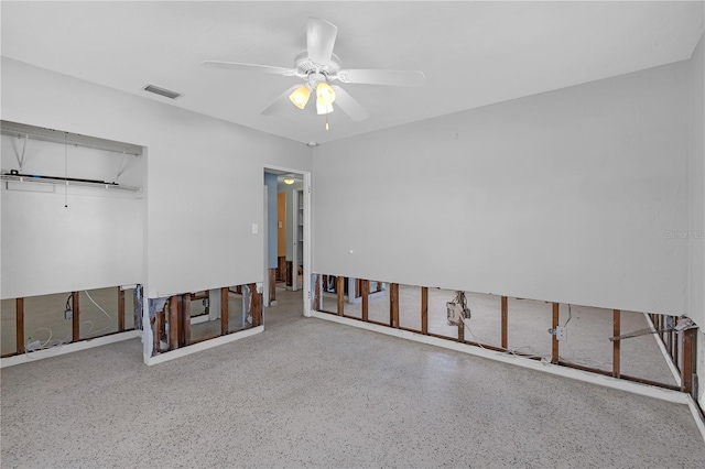 unfurnished room featuring ceiling fan, visible vents, attic access, and speckled floor