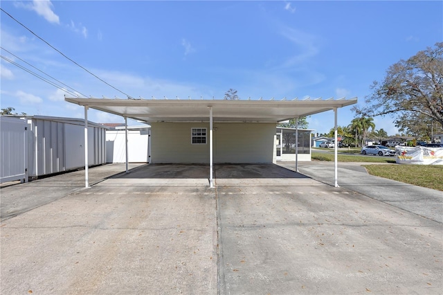 view of parking with driveway, an attached carport, and a shed