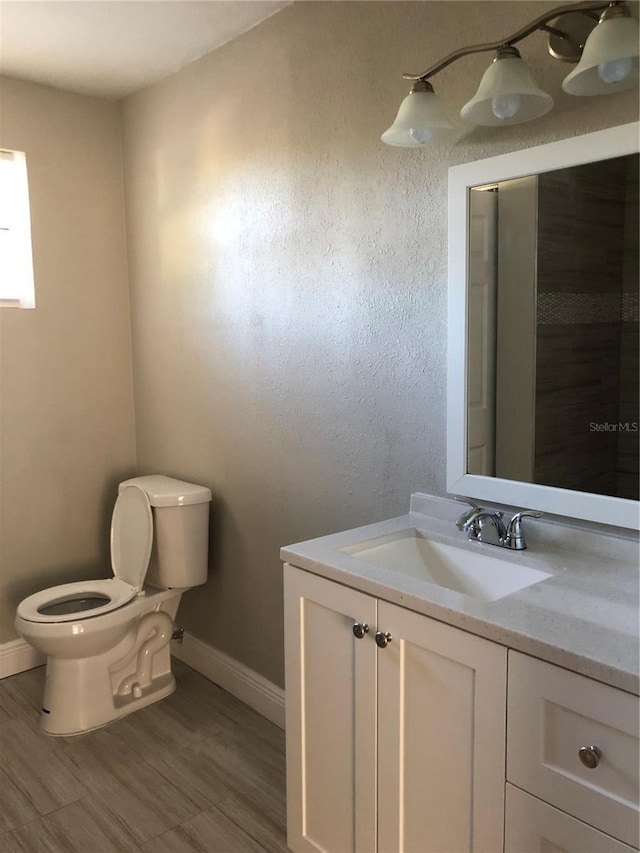 bathroom with toilet, wood finished floors, vanity, and baseboards