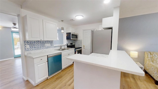 kitchen with decorative light fixtures, light countertops, appliances with stainless steel finishes, white cabinetry, and a sink