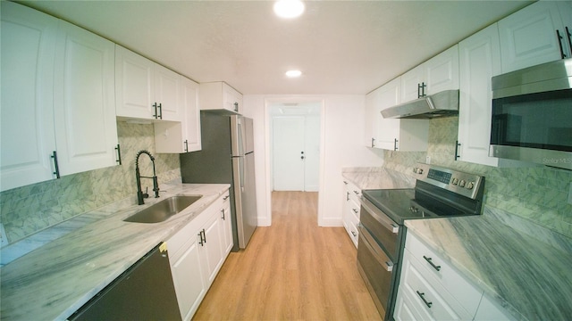 kitchen featuring under cabinet range hood, stainless steel appliances, a sink, white cabinetry, and light wood finished floors