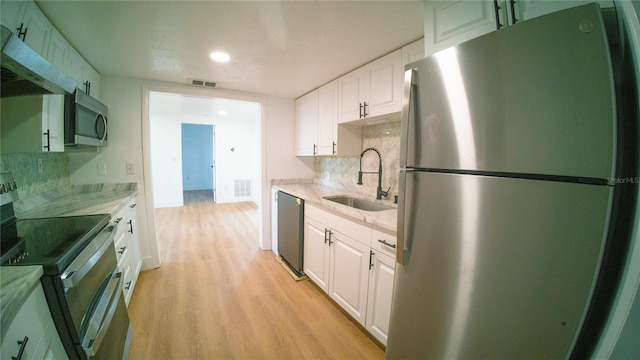 kitchen featuring visible vents, white cabinets, light wood-style flooring, stainless steel appliances, and a sink