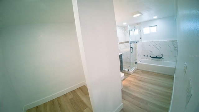 bathroom with a marble finish shower, baseboards, toilet, wood finished floors, and a bath