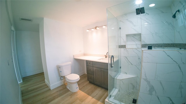 bathroom with a marble finish shower, visible vents, toilet, vanity, and wood finished floors