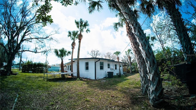 view of side of home with central air condition unit, a trampoline, a chimney, and a lawn