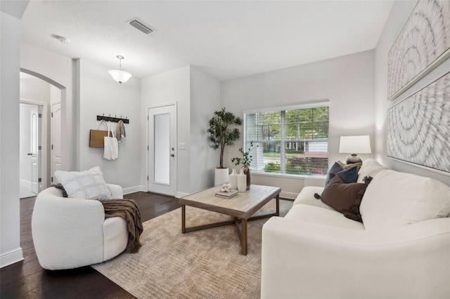 living room featuring baseboards, visible vents, arched walkways, and wood finished floors