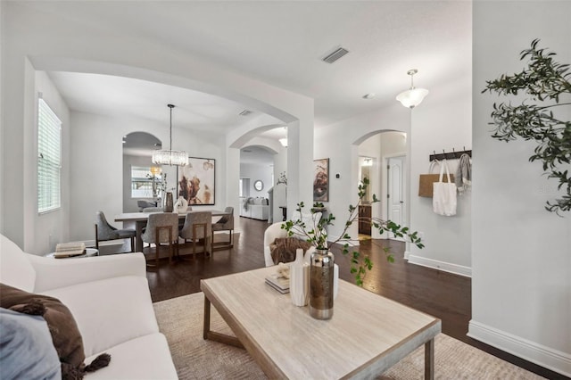 living room with baseboards, visible vents, arched walkways, wood finished floors, and a chandelier