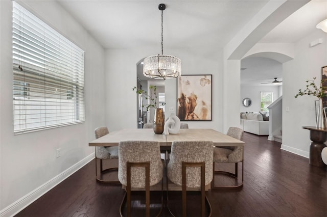 dining room featuring ceiling fan with notable chandelier, dark wood-type flooring, arched walkways, and baseboards