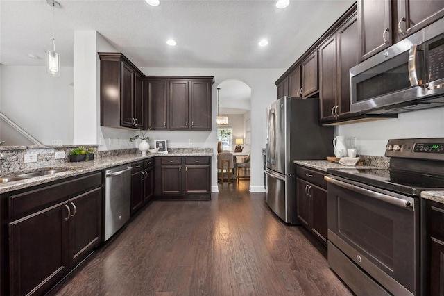 kitchen featuring dark brown cabinetry, arched walkways, stainless steel appliances, and a sink