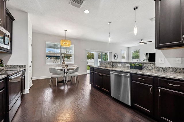 kitchen with dark wood-style flooring, visible vents, appliances with stainless steel finishes, light stone countertops, and decorative light fixtures