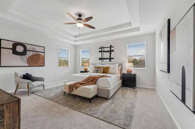 bedroom with a ceiling fan, a tray ceiling, carpet flooring, and baseboards