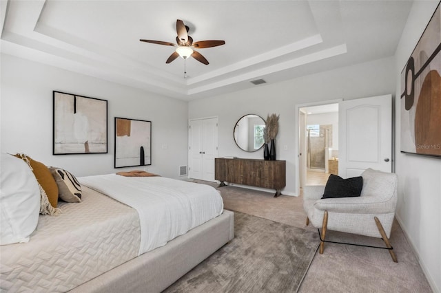 bedroom with baseboards, visible vents, a raised ceiling, connected bathroom, and light colored carpet