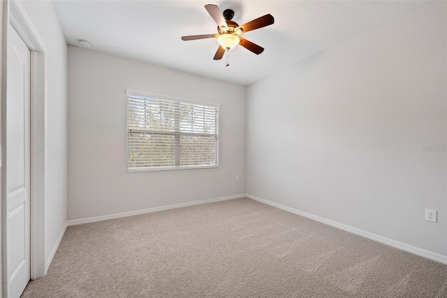 spare room featuring light colored carpet, ceiling fan, and baseboards