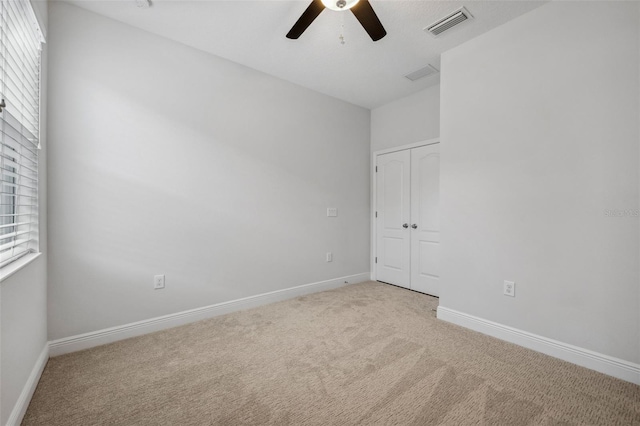 unfurnished bedroom featuring baseboards, visible vents, a ceiling fan, light colored carpet, and a closet