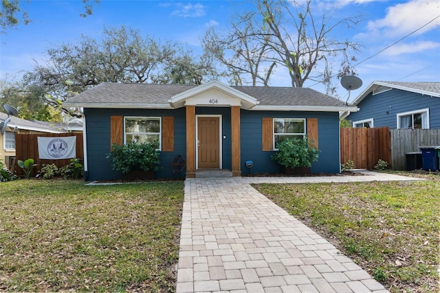 bungalow-style home featuring fence, a front lawn, and roof with shingles