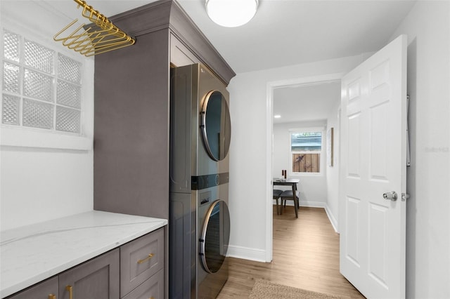 washroom featuring stacked washer / dryer, laundry area, baseboards, and light wood finished floors