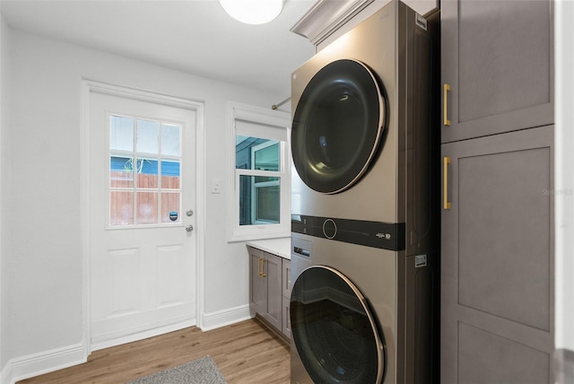 laundry room featuring baseboards, stacked washer / dryer, cabinet space, and light wood-style floors