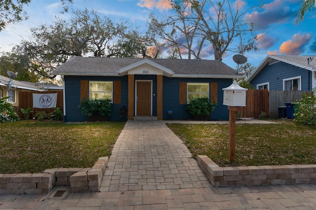 bungalow-style home featuring roof with shingles, a lawn, and fence