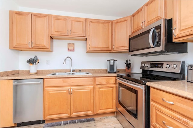 kitchen with appliances with stainless steel finishes, light countertops, a sink, and light brown cabinetry