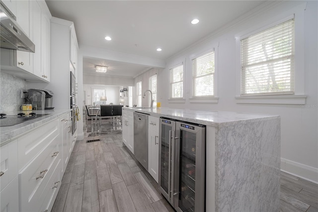 kitchen featuring wine cooler, black electric stovetop, a kitchen island with sink, dishwasher, and under cabinet range hood