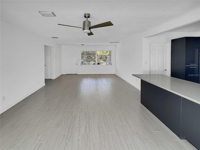 unfurnished living room with a textured ceiling, ceiling fan, visible vents, and light wood-style flooring