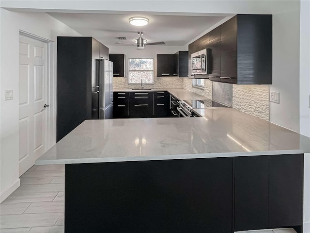 kitchen with a peninsula, a sink, appliances with stainless steel finishes, and dark cabinetry