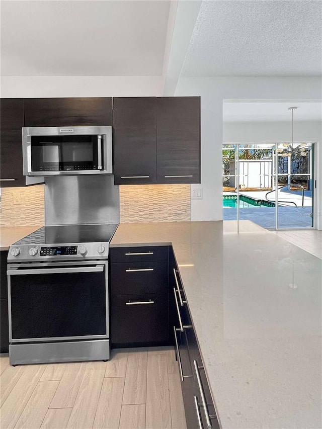 kitchen with appliances with stainless steel finishes, light wood finished floors, beamed ceiling, decorative light fixtures, and tasteful backsplash