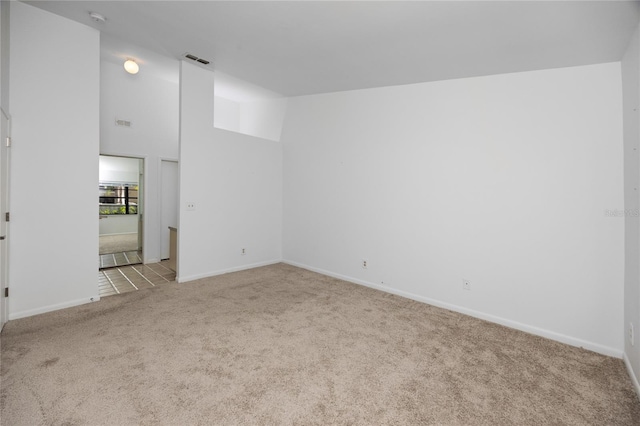 empty room featuring light carpet, lofted ceiling, visible vents, and baseboards