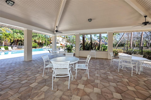 view of patio featuring a community pool, fence, a ceiling fan, and outdoor dining space