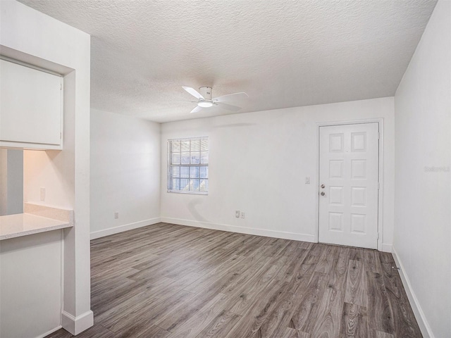 unfurnished room featuring baseboards, a textured ceiling, wood finished floors, and a ceiling fan