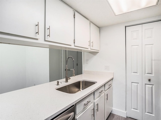 kitchen featuring a sink, baseboards, wood finished floors, white cabinets, and stainless steel dishwasher