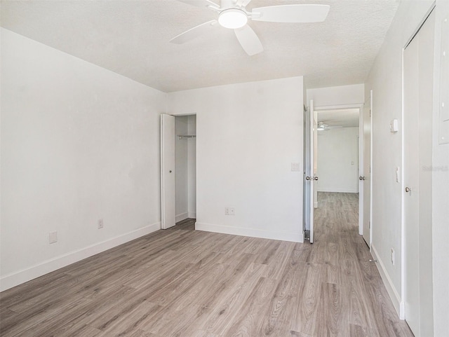 unfurnished bedroom with a textured ceiling, a closet, light wood finished floors, baseboards, and ceiling fan