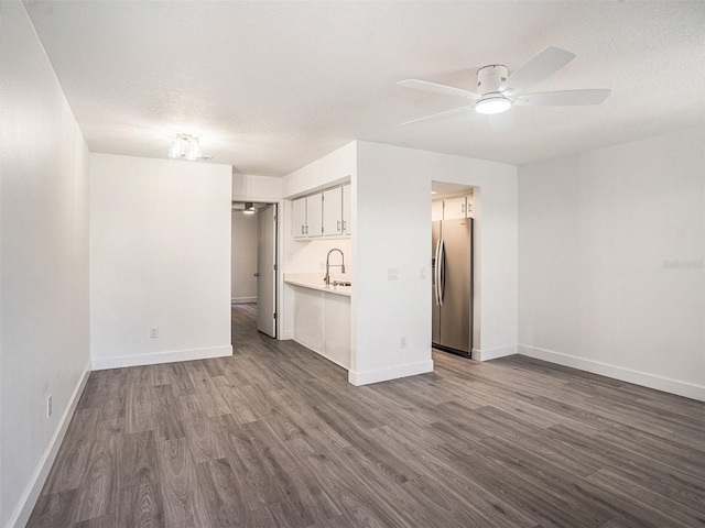 unfurnished living room featuring ceiling fan, dark wood-type flooring, baseboards, and a textured ceiling