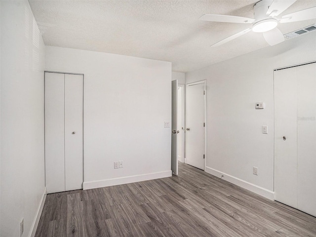 unfurnished bedroom with wood finished floors, baseboards, visible vents, multiple closets, and a textured ceiling